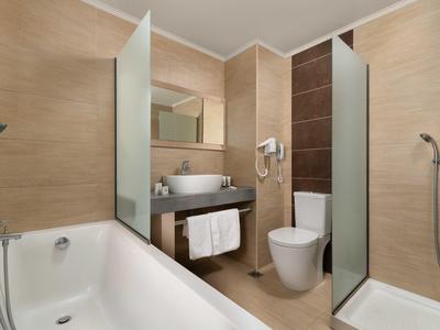 Bagno moderno in hotel con vasca, docce, wc, lavabo e pareti rivestite beige.