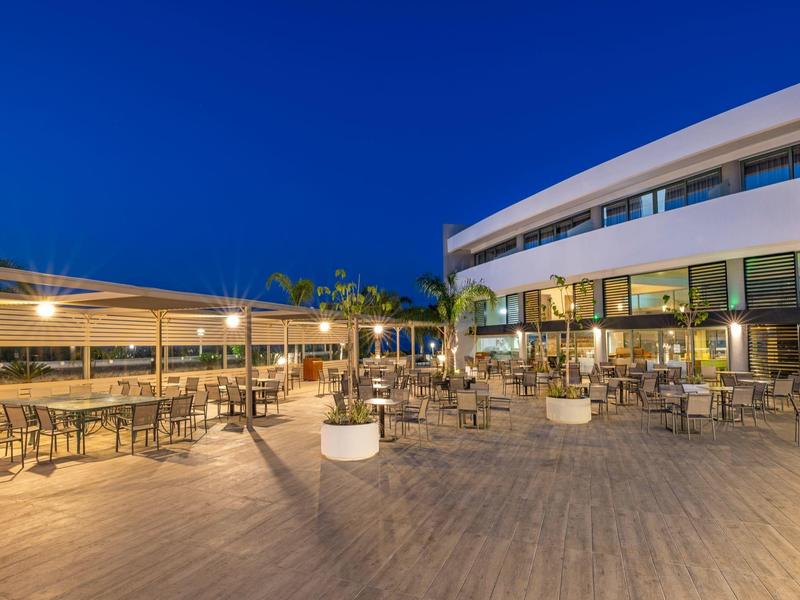 Terrazza esterna dell'hotel con tavoli e sedie illuminate di sera sotto un cielo blu chiaro.