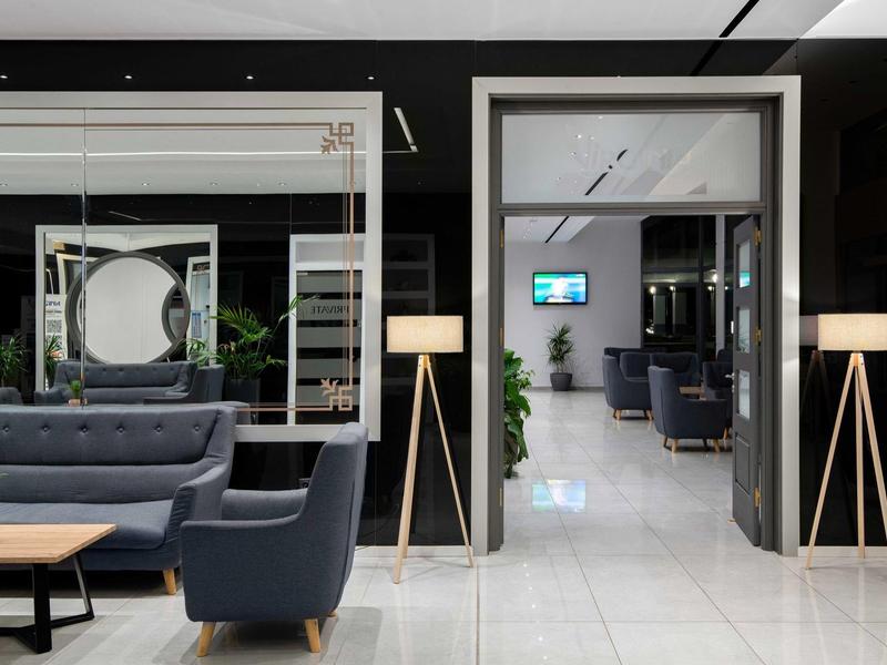 Lounge d'hotel moderno con divani grigi, pavimenti in marmo bianco e lampade eleganti.