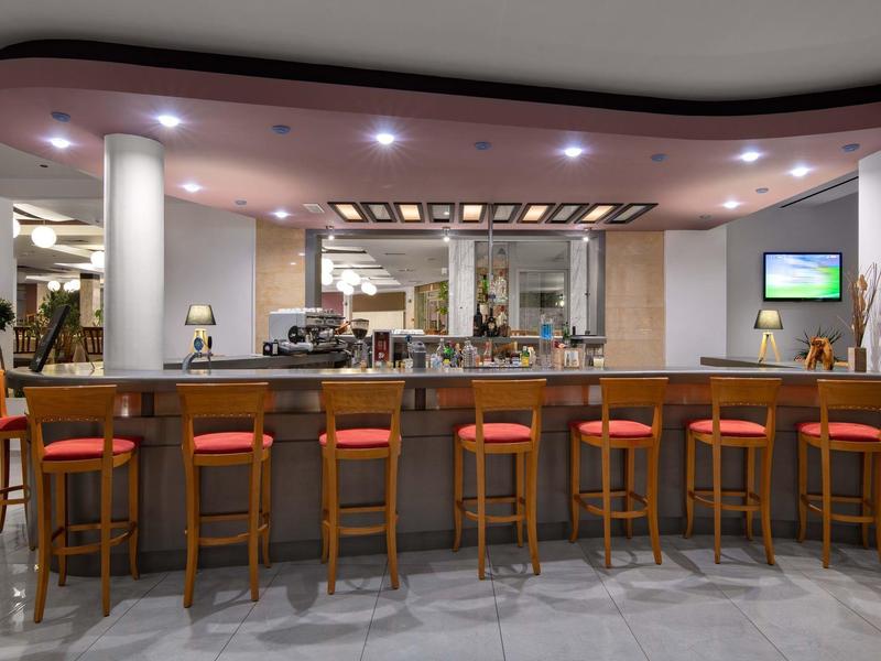 Bar dell'hotel moderno con sgabelli di legno e cuscini rossi sotto luci soffuse a soffitto.