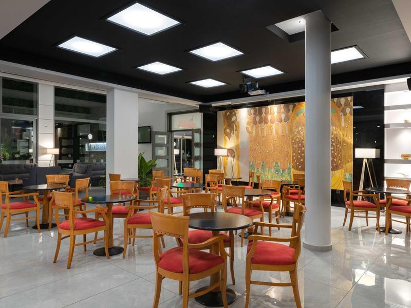 Sala da pranzo moderna dell'hotel con tavoli in legno, sedie imbottite rosse e illuminazione soffusa.