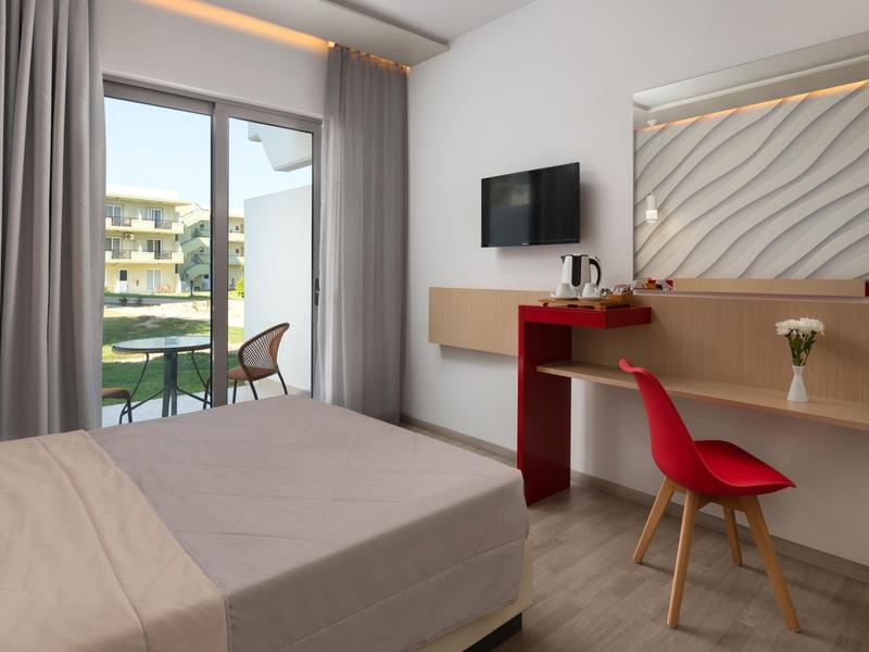 Camera d'hotel moderna con letto, sedia rossa, scrivania, TV e balcone con posti a sedere esterni.