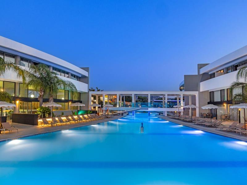 Piscina moderna dell'hotel al crepuscolo con lettini e acqua illuminata.
