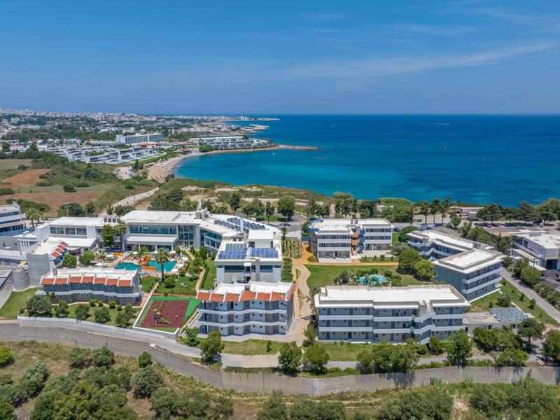 Resort costiero con edifici bianchi e piscine vicino al mare blu sotto un cielo limpido.