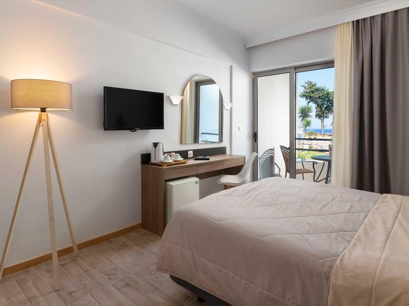 Camera d'hotel moderna con letto, scrivania, lampada da terra, TV e balcone con sedute esterne.