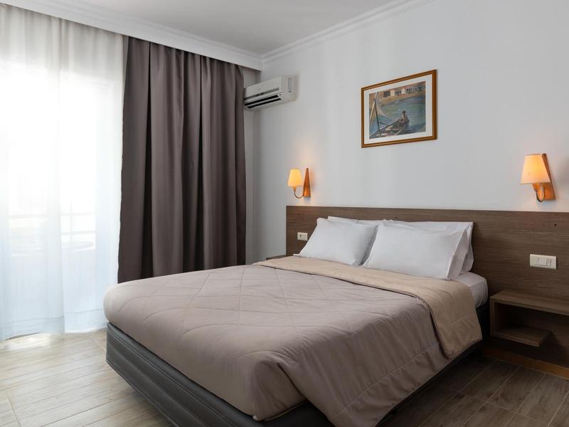 Camera d'hotel moderna con letto matrimoniale, lampade da comodino, aria condizionata e grande finestra con tende.