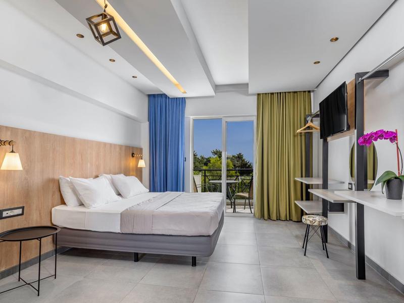 Camera d'hotel moderna con grande letto, testiera in legno, balcone e tende colorate.