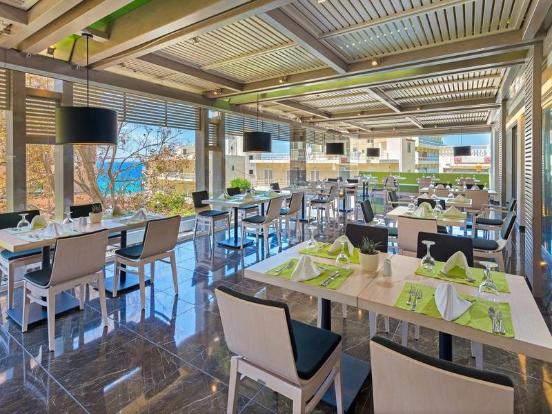 Bright, modern hotel restaurant with green napkins, large windows, and outdoor views.
