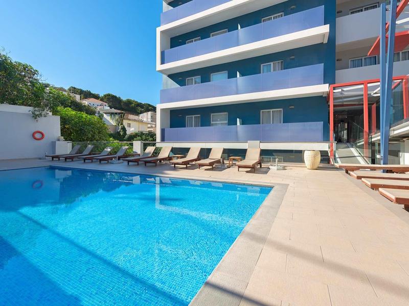 Outdoor pool with lounge chairs beside a modern hotel building under clear blue sky.