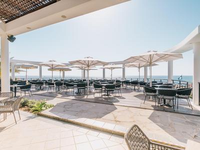 Terrasse avec tables, chaises et parasols avec vue sur la mer par une journée ensoleillée.