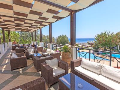 Terrasse ensoleillée avec sièges confortables, vue sur la piscine et la mer en arrière-plan.