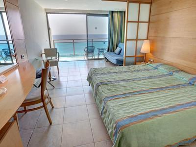 Camera d'hotel con letto matrimoniale, scrivania e balcone con vista mare.