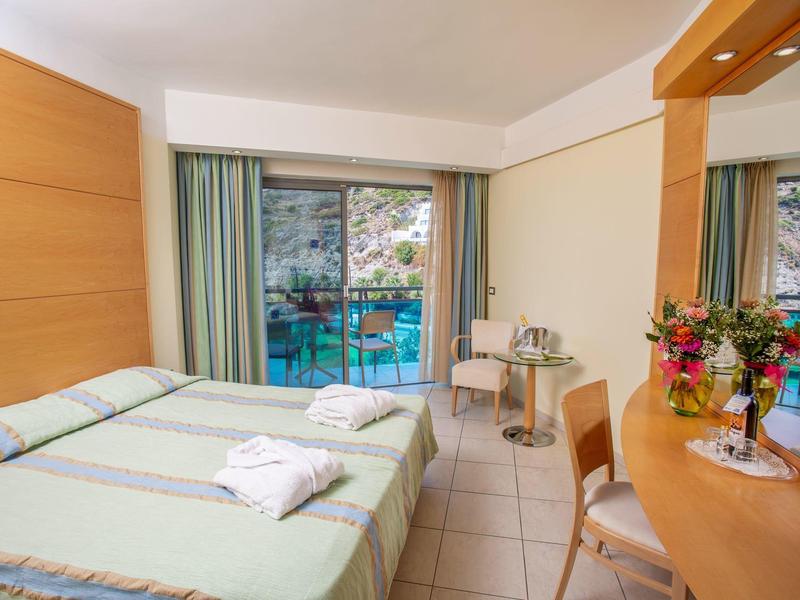 Camera d'hotel luminosa con due letti singoli, balcone e scrivania con fiori.