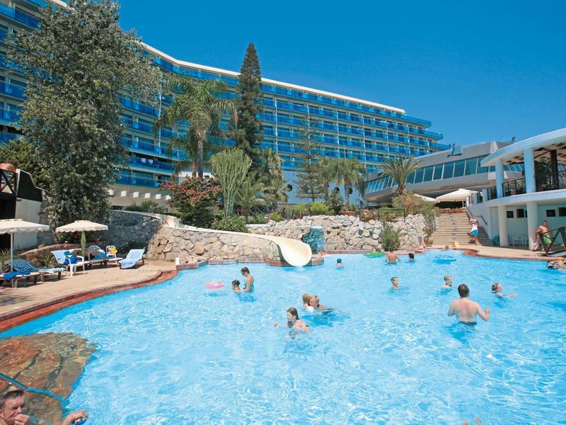 Piscina dell'hotel con persone, scivolo e ombrelloni sotto un cielo azzurro.