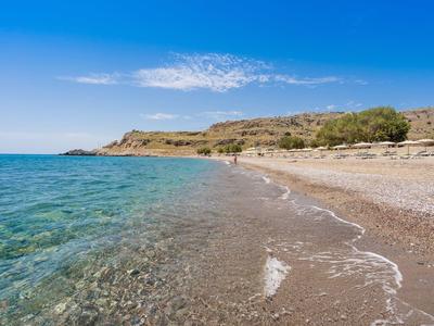 Przejrzysta plaża z kamienistym brzegiem i wzgórzami w tle pod błękitnym niebem.