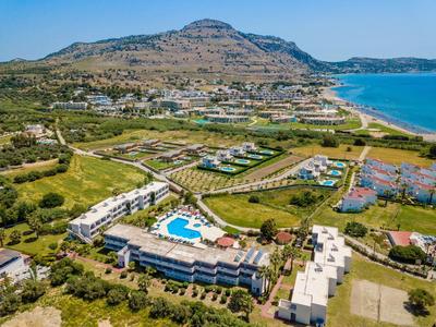 Widok na hotel z basenem, otoczony zielenią, górami i niebieskim morzem.