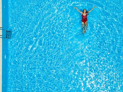 Osoba relaksująca się i pływająca w dużym, klarownym, niebieskim basenie na słońcu.