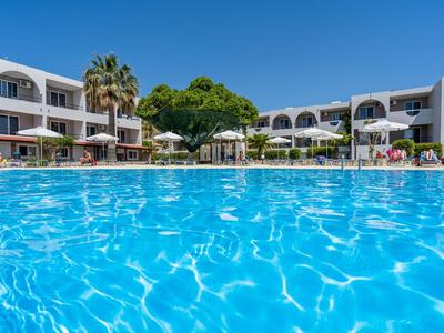 Duży basen z czystą wodą przed białym budynkiem hotelu pod niebieskim niebem.
