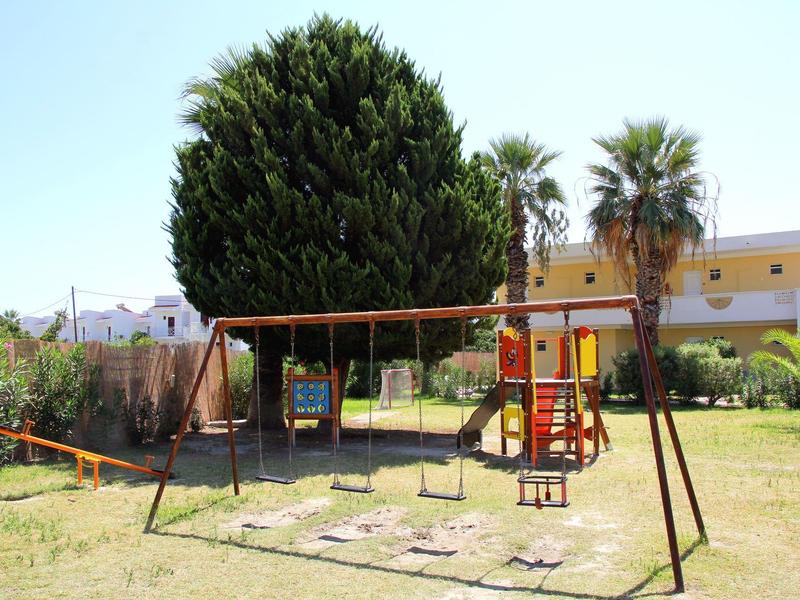 Plac zabaw dla dzieci z huśtawkami, zjeżdżalnią i drabinką na zielonej trawie przed żółtym budynkiem