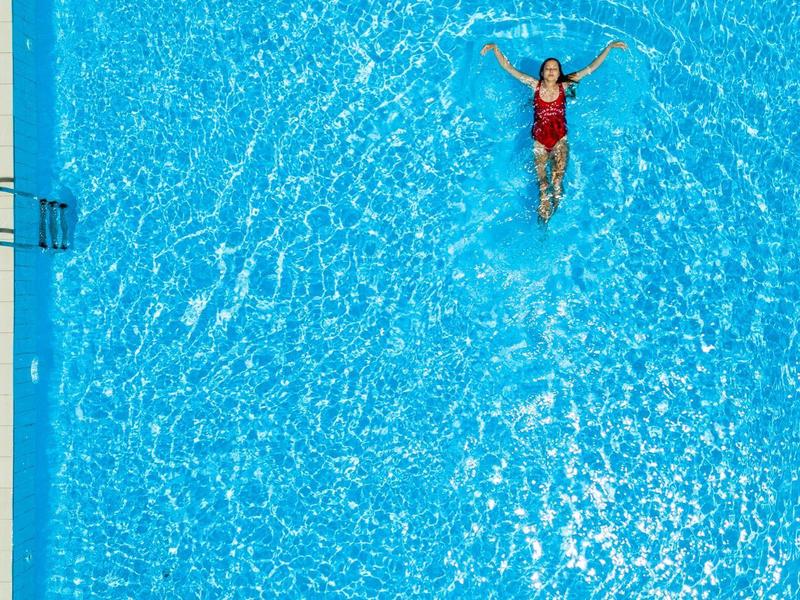 Mężczyzna pływa zrelaksowany w dużym, niebieskim basenie pod czystym niebem.