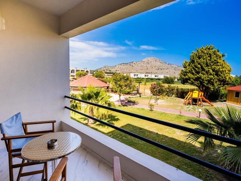 Balkon z krzesłem i stołem z widokiem na ogród i plac zabaw pod bezchmurnym niebem.