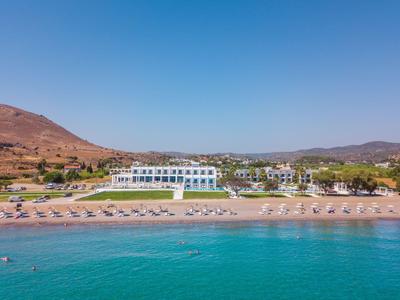 Playa con tumbonas frente a un hotel blanco y montañas al fondo bajo un cielo despejado.