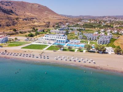View of a beach hotel with pool, sun umbrellas, and mountains in the background.