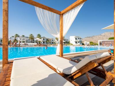 Tumbonas con cojines bajo un gazebo de madera junto a la piscina de un hotel en un día soleado.