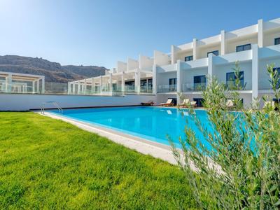 Complejo hotelero moderno con piscina, césped verde y cielo azul despejado.