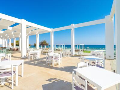 Terraza luminosa con mesas y sillas blancas, vista al mar y cielo despejado.