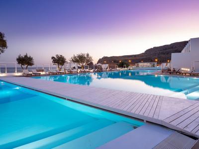Piscina de hotel iluminada al atardecer con vista a la montaña y zona de descanso.