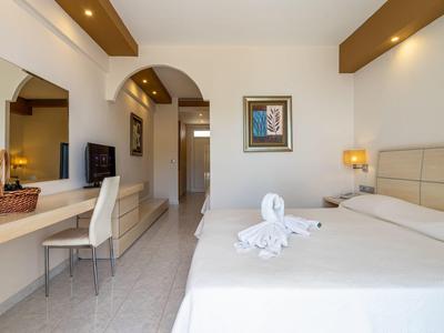 Bright hotel room with large bed, mirror, TV, and decorative towel on the bed.