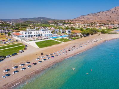 Beachfront hotel resort with umbrellas and clear blue water near mountains.