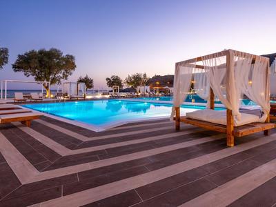 Área moderna de piscina con camas de madera y vista al mar al atardecer.