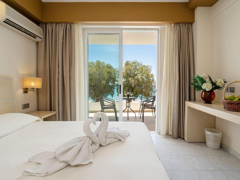 Hotel room with double bed, balcony, and sea view with trees.