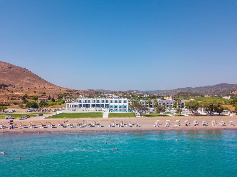 Hotel complex with white building, sun loungers on the beach, and clear blue water.