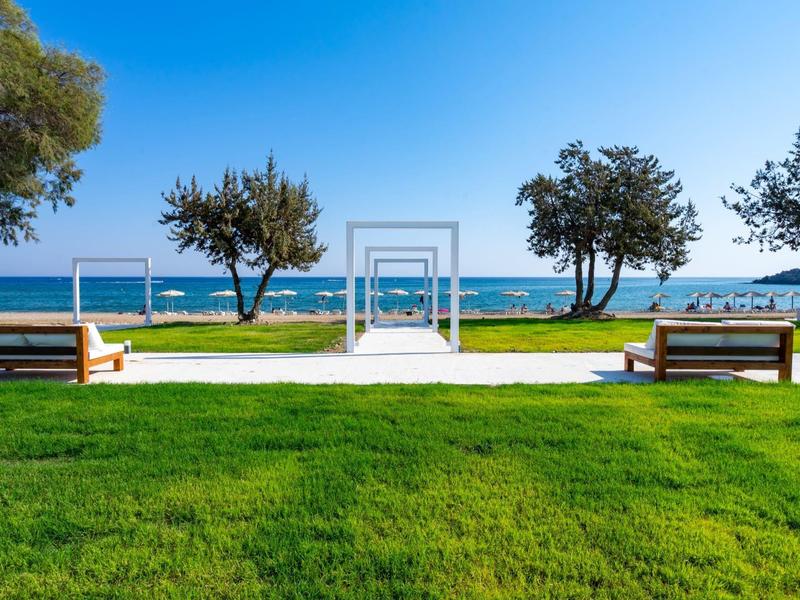 Green lawn with benches and archway by the sea under a blue sky.