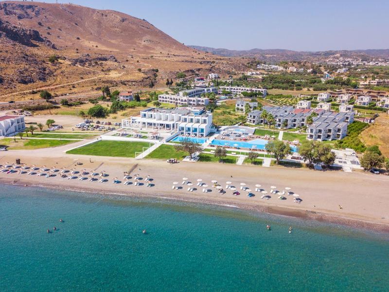 View of a beach hotel with pool, sun umbrellas, and mountains in the background.