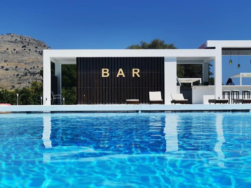 Modern pool with clear blue water and bar in the background under blue sky.