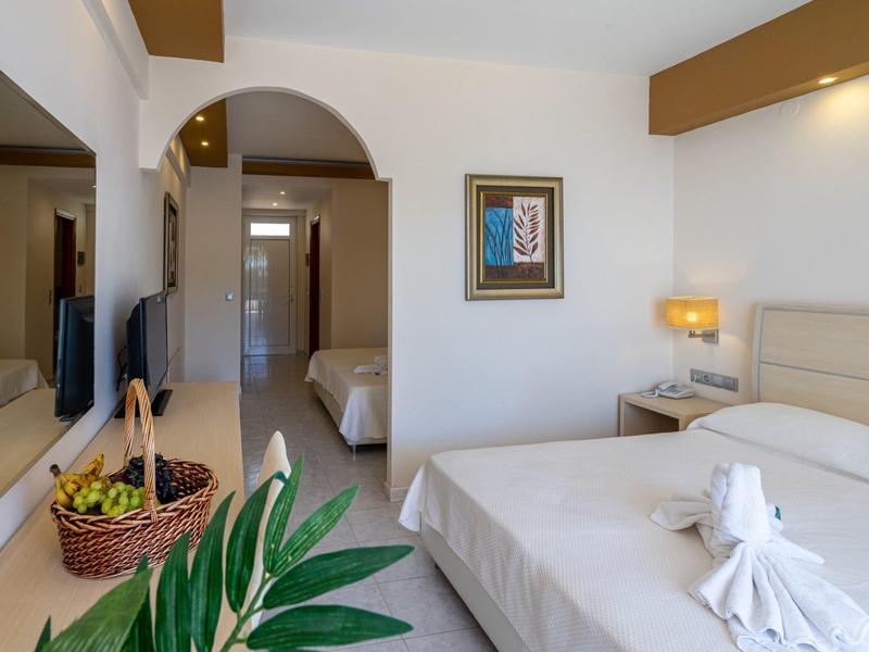 Brightly furnished hotel room with double bed, TV, and view into adjoining room.