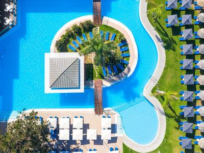 Vogelperspektive eines Hotelpools mit Liegestühlen und Sonnenschirmen in einer tropischen Anlage.