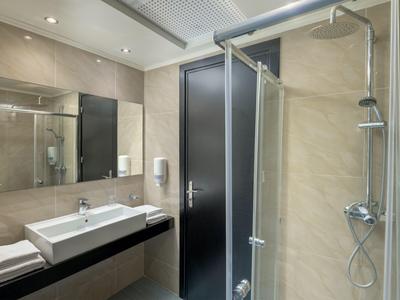 Modern hotel bathroom with shower, sink, and towels in neutral colors.