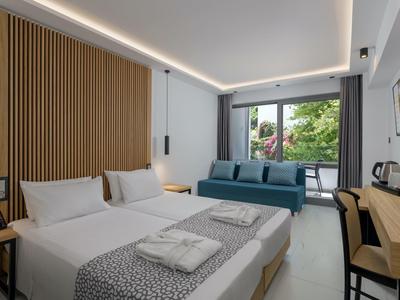 Camera d'hotel moderna con letto matrimoniale, divano, scrivania e balcone con vista su alberi verdi.