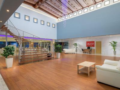 Heller, moderner Hotellobby mit Holzfußboden, weißen Sofas und einer Treppe zum Obergeschoss.