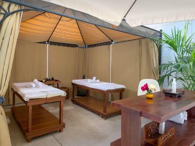 Area relax con due lettini da massaggio in una tenda aperta con mobili in legno e piante.