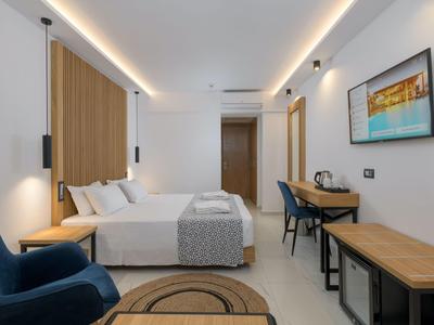 Modern hotel room with double bed, desk, armchairs, and wall art in neutral tones.
