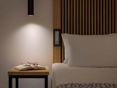 Comodino illuminato con libro e occhiali accanto a letto moderno in camera d'hotel.