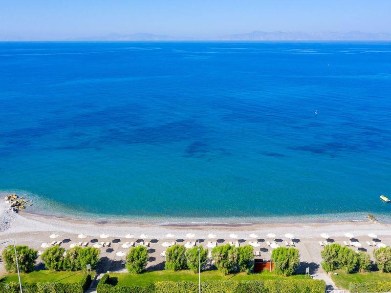 Spiaggia con ombrelloni e lettini vicino a un mare blu chiaro, alberi verdi in primo piano