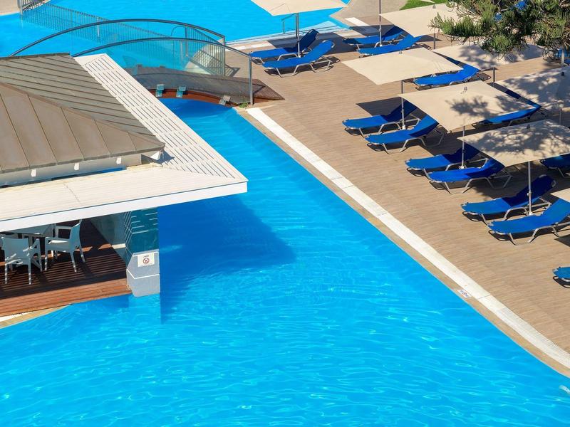 Area piscina moderna con lettini blu e ombrelloni accanto all'acqua limpida.