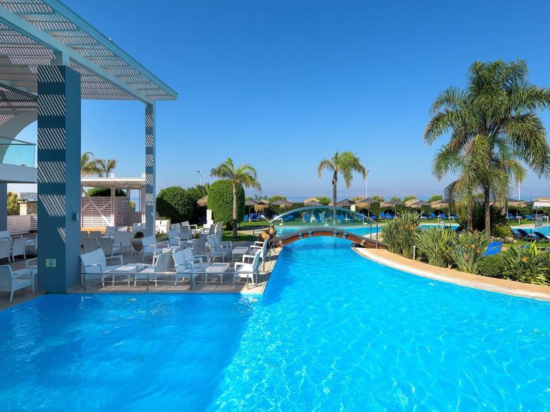 Una piscina all'aperto di lusso con sedie a sdraio e palme sotto un cielo sereno.